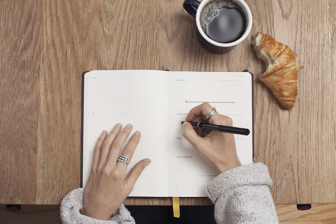 Someone writing in a planner next to a cup of coffee